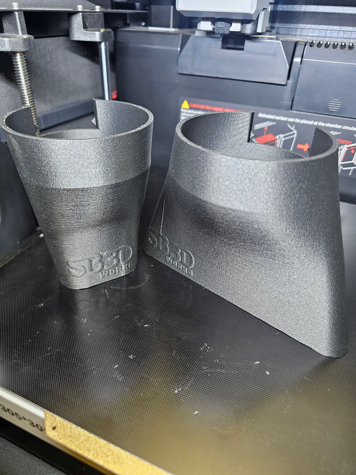 SB3DWorksin 3D-tulostama suutinsetti Ryobi ONE+ HP Brushless -lehtipuhaltimeen, kaksi harmaata suutinta 3D-tulostimen alustalla